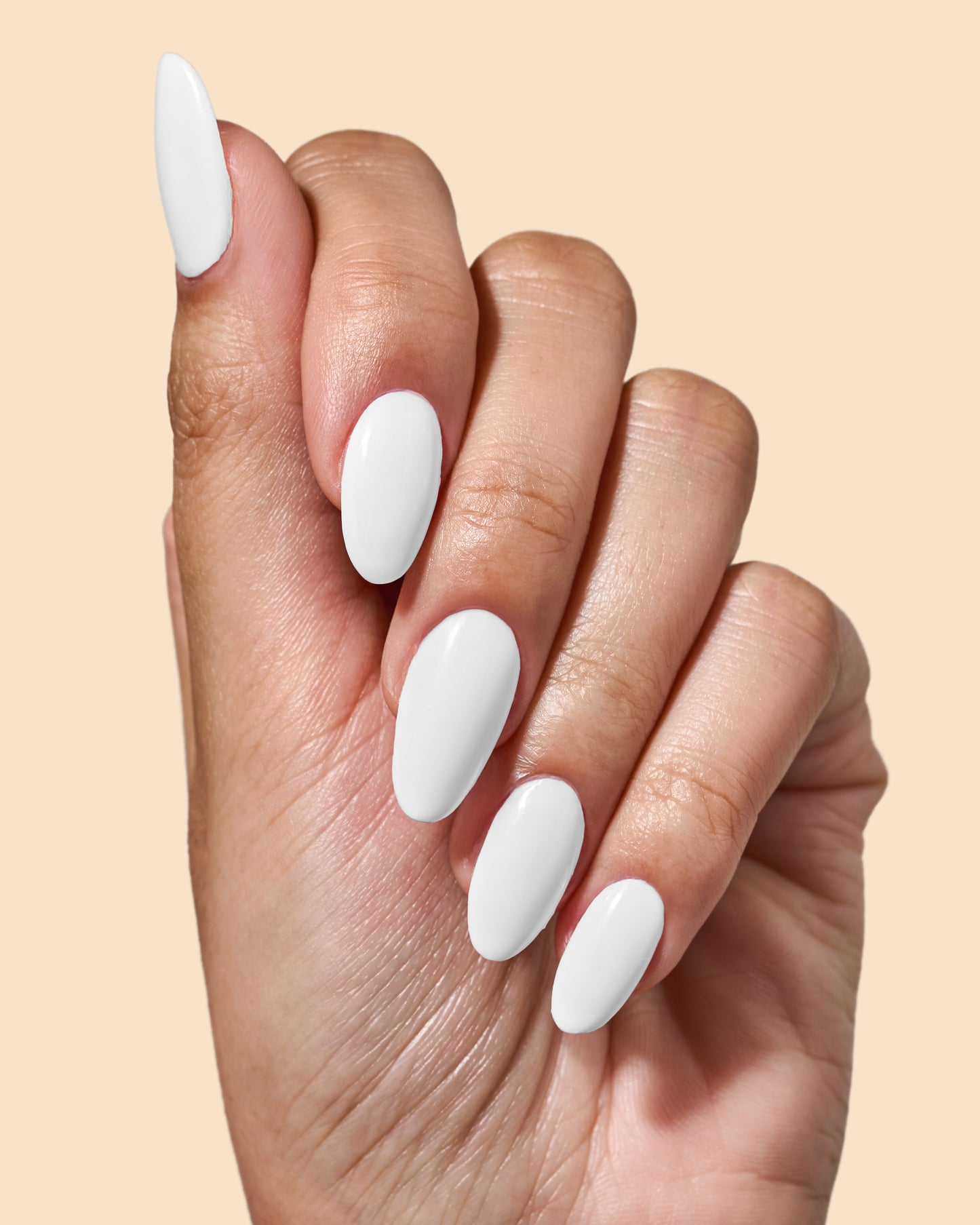 A close-up of a hand with long, almond-shaped nails painted in a glossy white manicure, set against a solid light beige background.