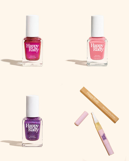 Three Happy Rudy nail polish bottles in pink, red, and purple shades, alongside a lip gloss tube and its wooden box, arranged on a light beige background.