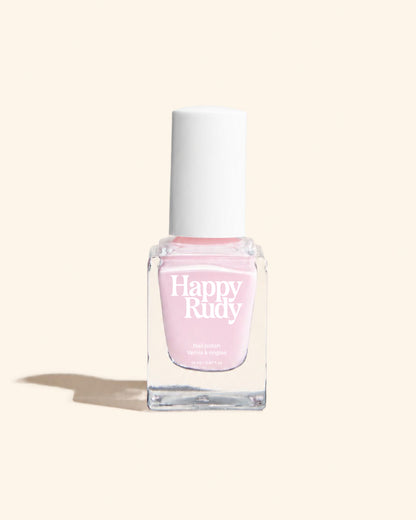 A bottle of Happy Rudy nail polish in a light pink shade, featuring a clear glass bottle and a white cap, set against a solid cream background with a soft shadow.