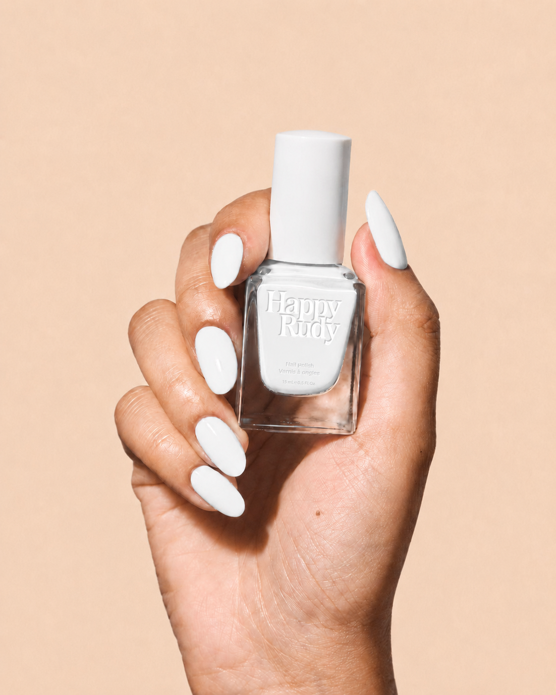 A hand with long, glossy white manicured nails holds a bottle of Happy Rudy white nail polish against a solid beige background.