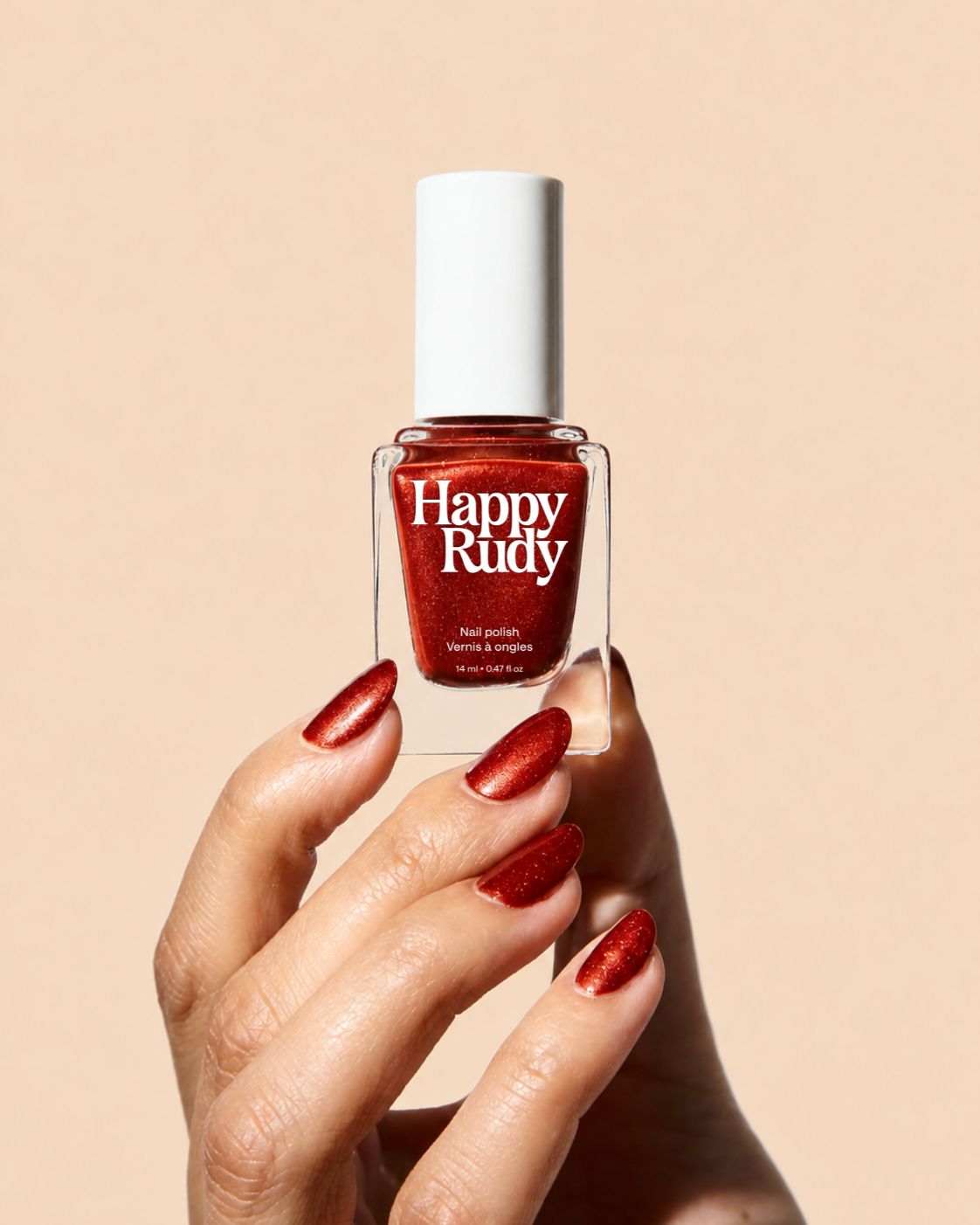 A hand with metallic brown nail polish holds a bottle of Happy Rudy nail polish against a solid beige background.