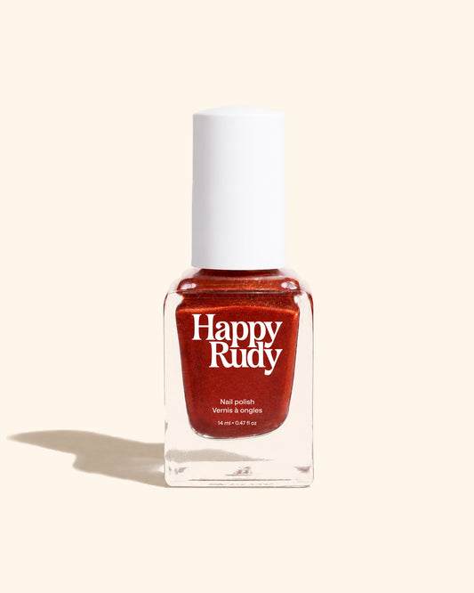 A bottle of Happy Rudy nail polish in a warm, shimmery coppery red shade, set against a solid cream background with a soft shadow.