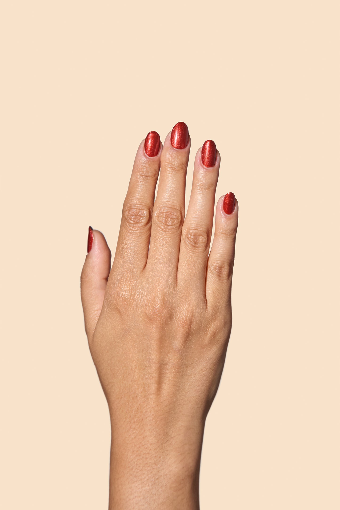 Hand with brown shimmer nail polish on a beige background