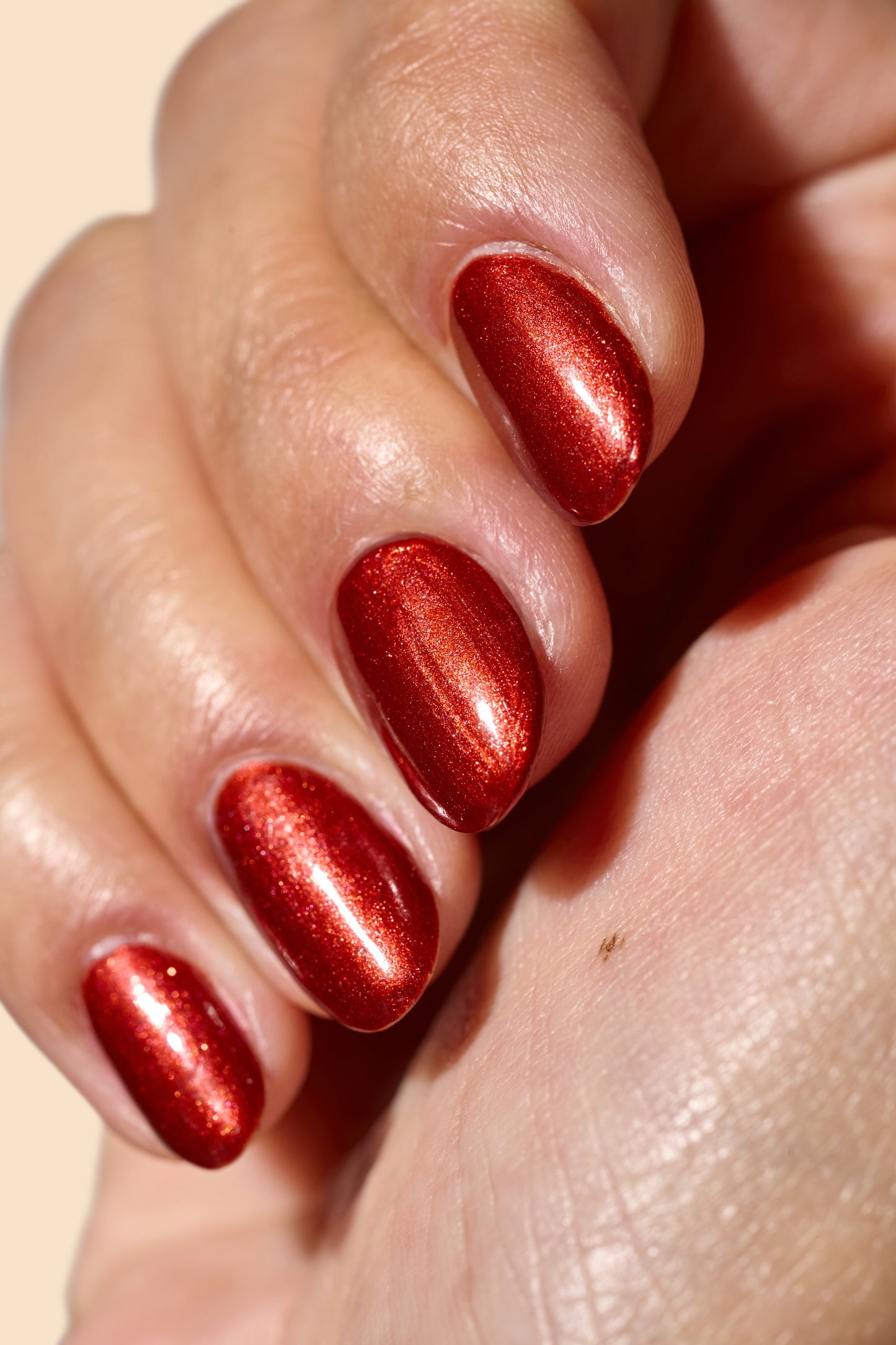 Close-up of a hand with brown metallic nail polish on a beige background