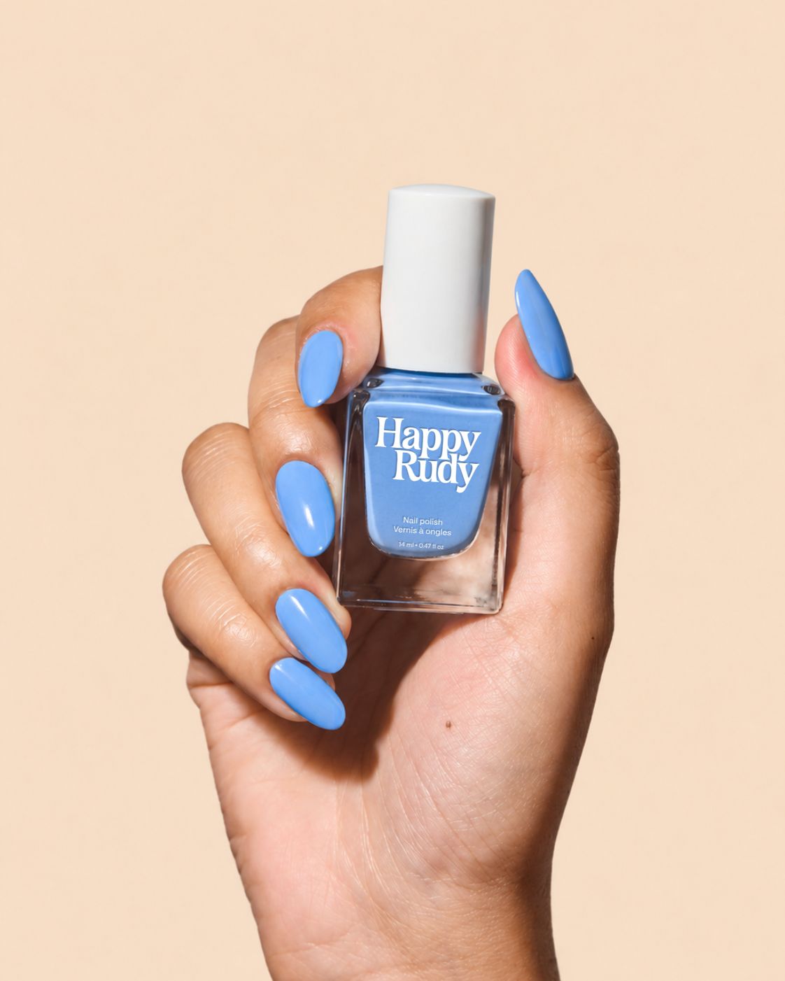 A hand with long, glossy light blue manicured nails holds a bottle of Happy Rudy nail polish against a solid beige background.