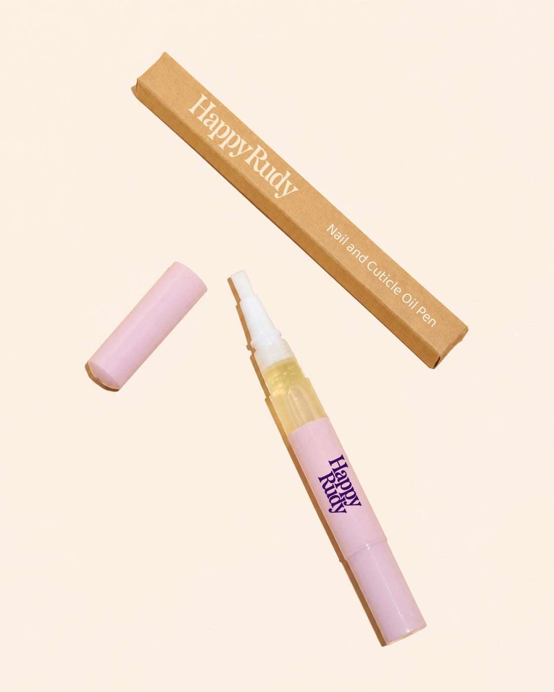 HappyRudy Nail and Cuticle Oil Pen shown with its cap off and its kraft paper packaging box on a solid pale beige background.