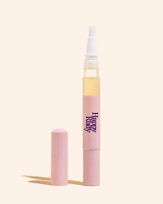 A pink cosmetic tube with a white applicator tip and a separate pink cap, shown on a warm off-white background. The tube has the text 'Happy Happy' printed vertically in purple.