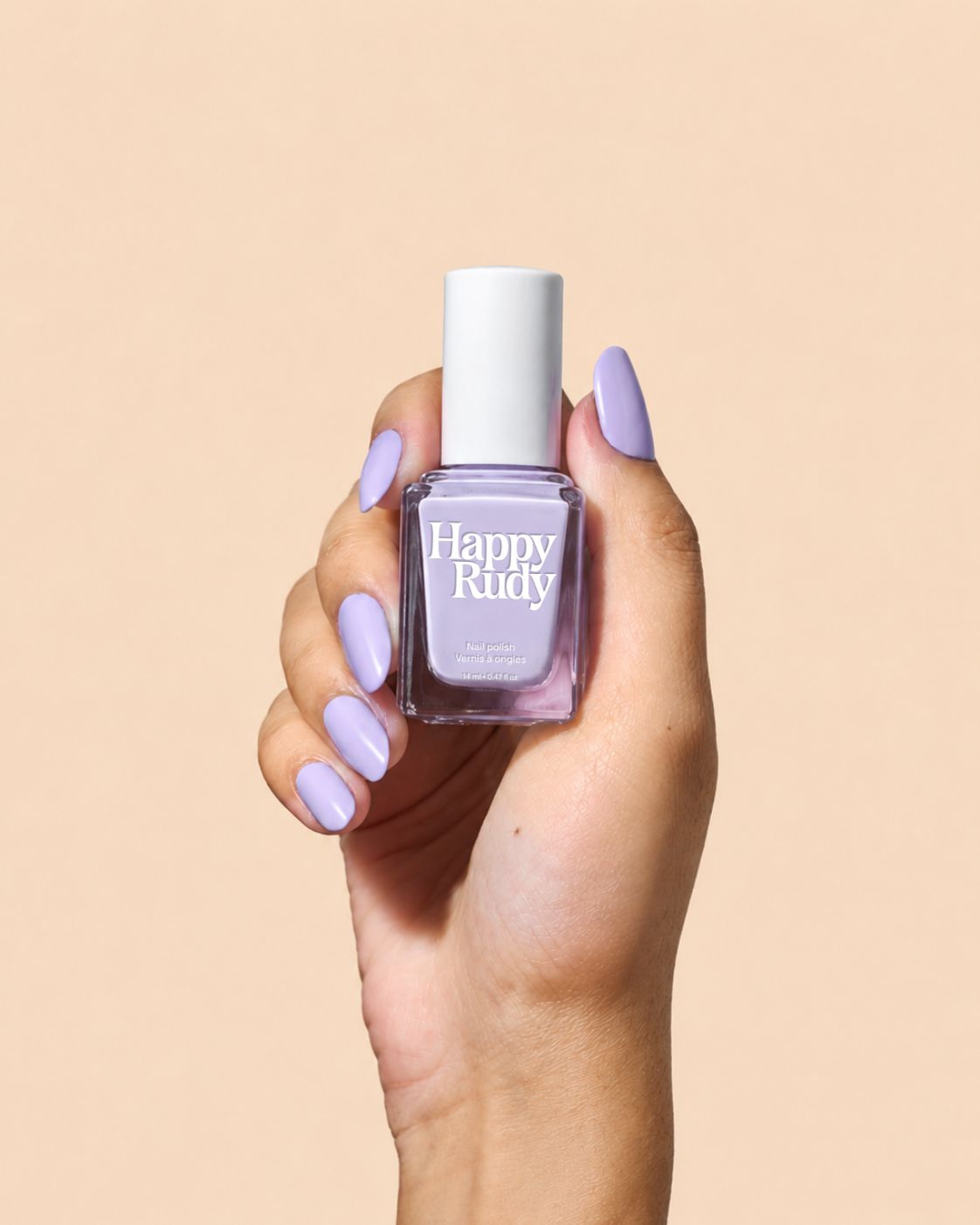 A hand holding a bottle of Happy Rudy nail polish, showcasing a light lavender purple shade. The hand has matching lavender nails, and the background is a solid, warm beige color.