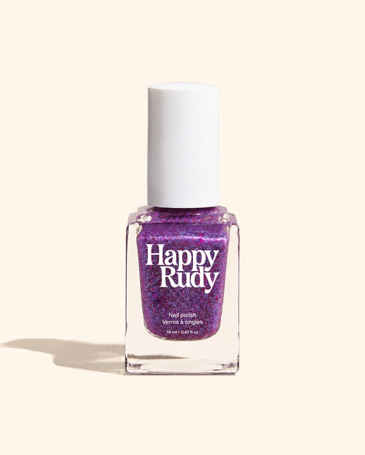 A bottle of Happy Rudy nail polish in a vibrant purple glitter shade, shown against a solid cream background with a soft shadow.